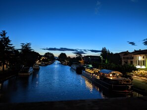 A canal with boats, buildings on the right, and trees on the left.