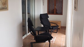 Un espacio habitable pequeño y de concepto abierto, con un ventanal corredera que da a un balcón, un banco de madera y dos sillas negras.
