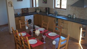 Una cocina con armarios de madera, lavadora integrada, una mesa de comedor preparada para cuatro personas y un ventanal que proporciona luz natural.