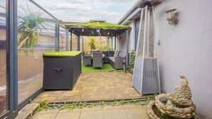 A glass-enclosed patio with outdoor furniture, a green roofed pergola, and a decorative stone sculpture. - Holiday Home in Verviers with Sauna (Verviers)