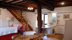 Ein gemütliches Wohnzimmer mit einem roten Sofa, einer Holztreppe und einem Essbereich mit Tisch und Stühlen.