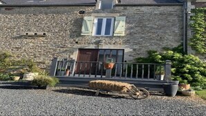 Ein Steinhaus mit einer Holzveranda, einem Fenster mit Fensterläden und einem Heuballen auf dem Boden.