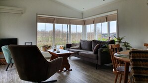 A spacious living room with a large window, a sofa, a dining table, and a TV. - Canal-Side Stay, Giethoorn (Giethoorn)