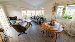A spacious living area with a sofa, armchair, and dining table. There is a TV, a plant, and a window with curtains. - Canal-Side Stay, Giethoorn (Giethoorn)