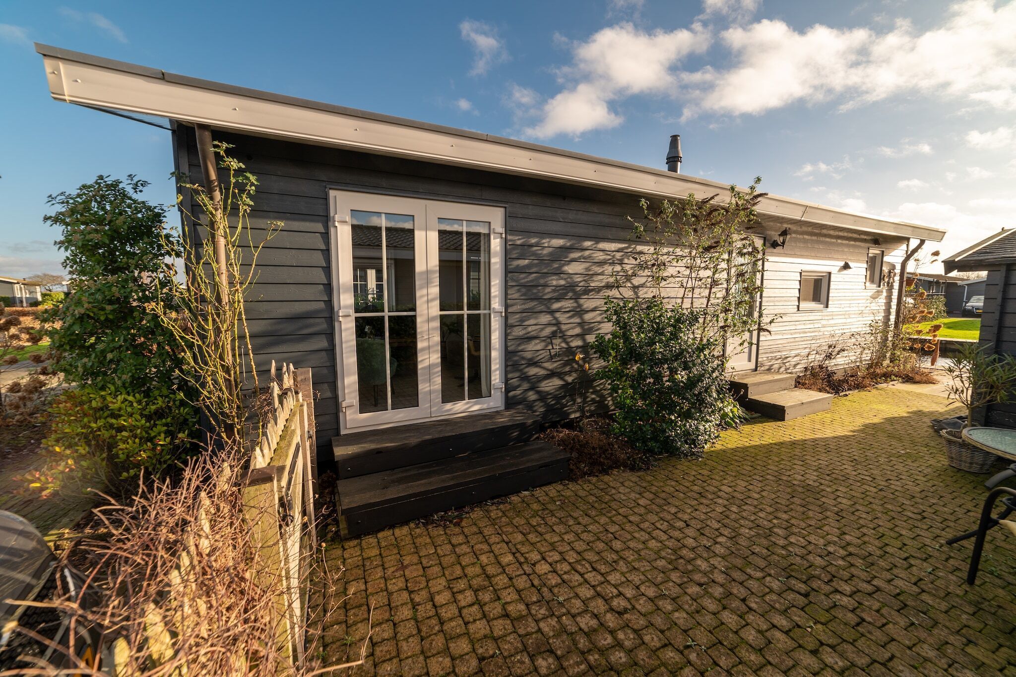 Een gelijkvloers huis met een donkere gevel, een voordeur met witte omlijsting en een klein portiek.