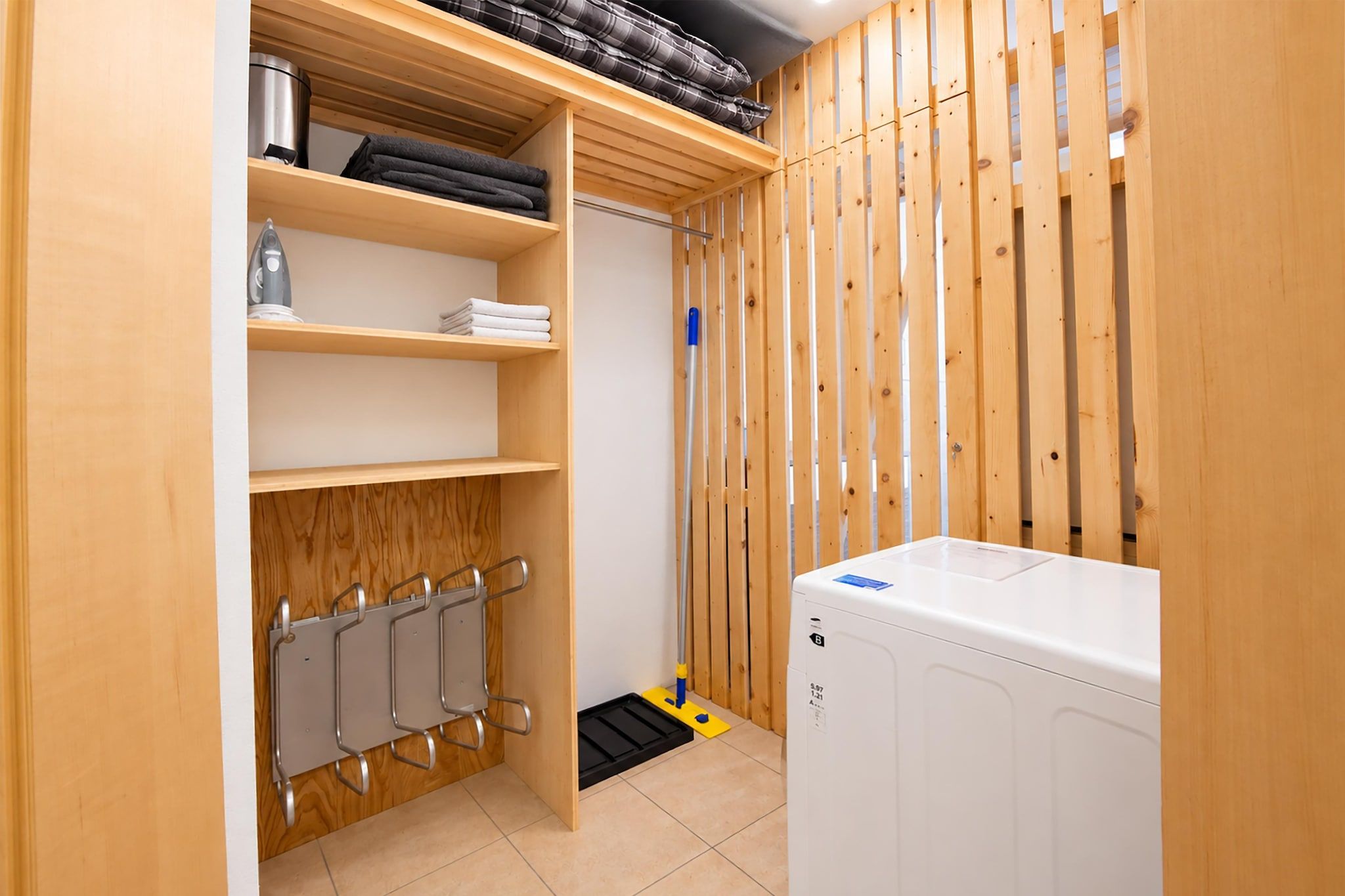 A laundry room with a washing machine, shelves with folded towels, and a mop.