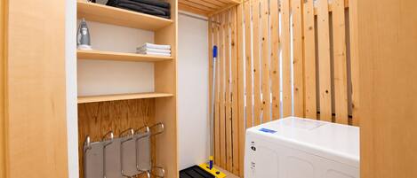 A laundry room with a washing machine, shelves with folded towels, and a mop.