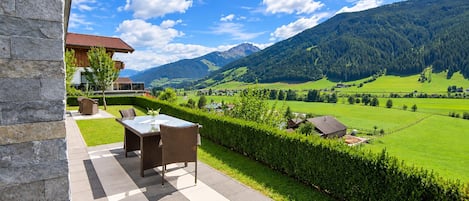 A patio with a table and chairs, a stone wall, and a view of a green valley with mountains.