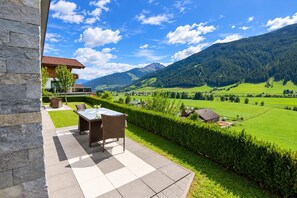 A patio with a table and chairs, a stone wall, and a view of a green valley with mountains.