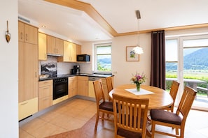 A modern kitchen with wooden cabinets, a dining table with chairs, and a view of mountains through large windows.