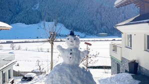 Un bonhome de neu en un paisatge hivernal nevós, amb una casa al fons.
