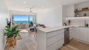 Una cocina moderna con armarios blancos, lavavajillas y vista al océano a través de un ventanal corredero.