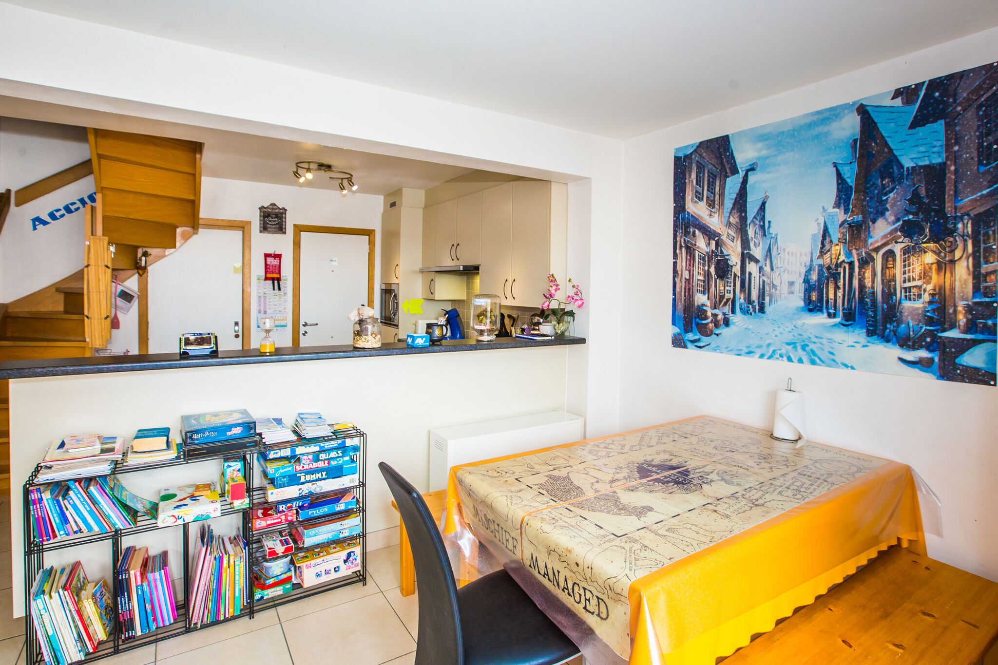 Una habitación acogedora con una mesa de comedor, una estantería y un cuadro que muestra una calle nevada.