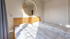 A neatly made bed with a wooden headboard, a round mirror on the wall, and a bedside lamp. - Duplex apartment near the sea (Middelkerke)
