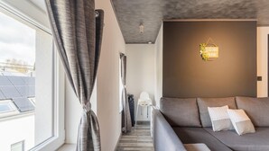 A modern living room with a grey sofa, a 'Welcome Home' sign, and a view of solar panels outside.