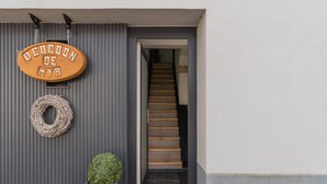 A wooden sign with text, a wreath, and a potted plant at the entrance of a building.