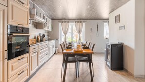 A modern kitchen with a dining area, featuring a built-in oven, a refrigerator, and a dining table set for six.