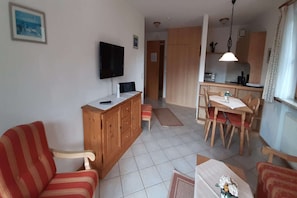Una sala de estar con un sofá, un aparador de madera, un televisor y un comedor con una mesa y sillas.