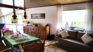 Una sala de estar acogedora con una mesa de comedor, sillas de madera, un sofá y una ventana con cortinas.