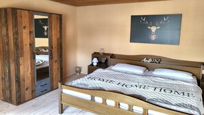 Un dormitorio con cama de madera, un armario con espejo, una mesita de noche, un cuadro en la pared de un ciervo y una lámpara de techo.