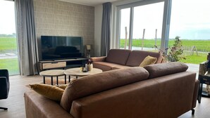 A modern living room with a leather sofa, a flat-screen TV, and a small round table. - Villa in Friesland with Boat Rental (Leons)