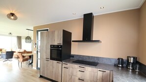 A modern kitchen with wooden cabinets, a black range hood, and a countertop with a coffee maker. - Villa in Friesland with Boat Rental (Leons)
