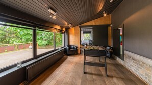 A room with a foosball table, large windows, and a view of greenery outside.