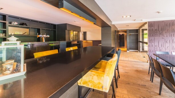 A modern kitchen with a long island, bar stools, and a dining area with a dark table and chairs.