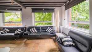 A modern living room with a sectional sofa, large windows, and a tiled floor.