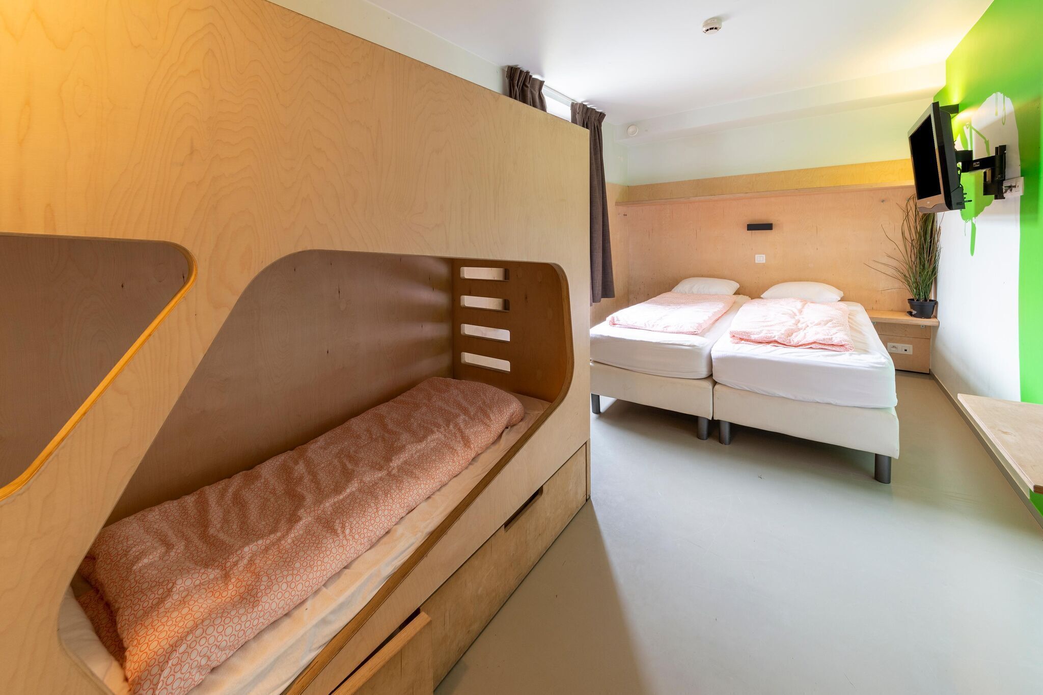 Ein Zimmer mit einem Etagenbett, einem Doppelbett, einem an der Wand montierten Fernseher und einem kleinen Tisch.