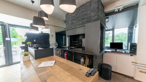 A modern kitchen with a wooden countertop, hanging pendant lights, a built-in oven, and a large window overlooking greenery. - Holiday Home in Durbuy near Adventure Valley (Durby)