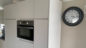 Une cuisine avec des meubles blancs, un four encastré et une horloge murale.