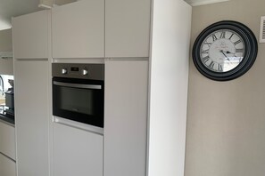 A kitchen with white cabinetry, a built-in oven, and a wall-mounted clock.