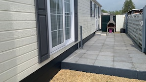 Une maison mobile moderne dotée de grandes fenêtres, d’un espace patio et d’un four en briques.