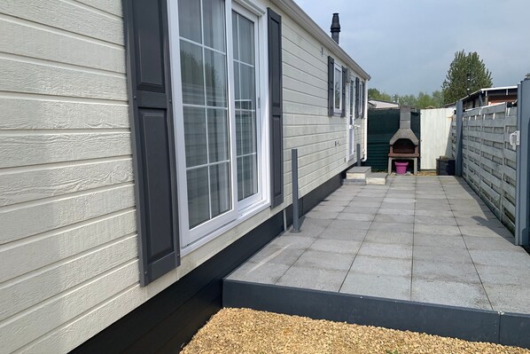 A modern mobile home with large windows, a patio area, and a brick oven. - Wonderful Holiday Home in Nieuwpoort near Dunepark (Nieuwpoort)