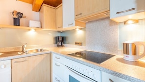 A modern kitchen with white cabinets, a stainless steel sink, a built-in stove, and a coffee maker. - Chalet in Gattererberg near Ski Slopes (Stummerberg)
