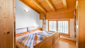 A wooden cabin bedroom with a bed, a nightstand, and a window with curtains. - Chalet in Gattererberg near Ski Slopes (Stummerberg)