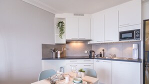 A modern kitchen with white cabinets, a microwave, and a sink. There is a dining table set with plates, glasses, and cutlery.