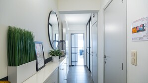 A hallway with a potted plant, a framed menu, a mirror, and a door leading to a bright room.