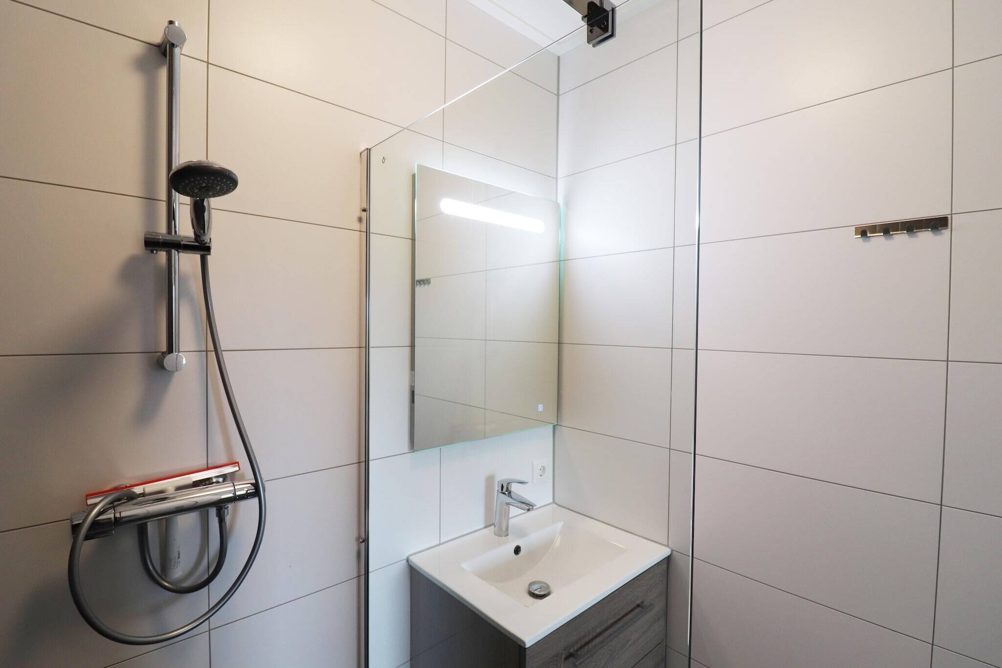 Une salle de bain moderne avec une douche à parois de verre, un lavabo blanc et un miroir.