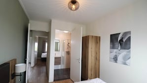 A hotel room with a bed, a bedside table, a lamp, a wooden wardrobe, and a bathroom visible through an open door. - Villa in Leons with Sloop Rental (Leons)