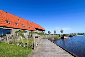 Un muelle de madera que conduce a un canal con un bote, un edificio de techo rojo y un cielo azul despejado.