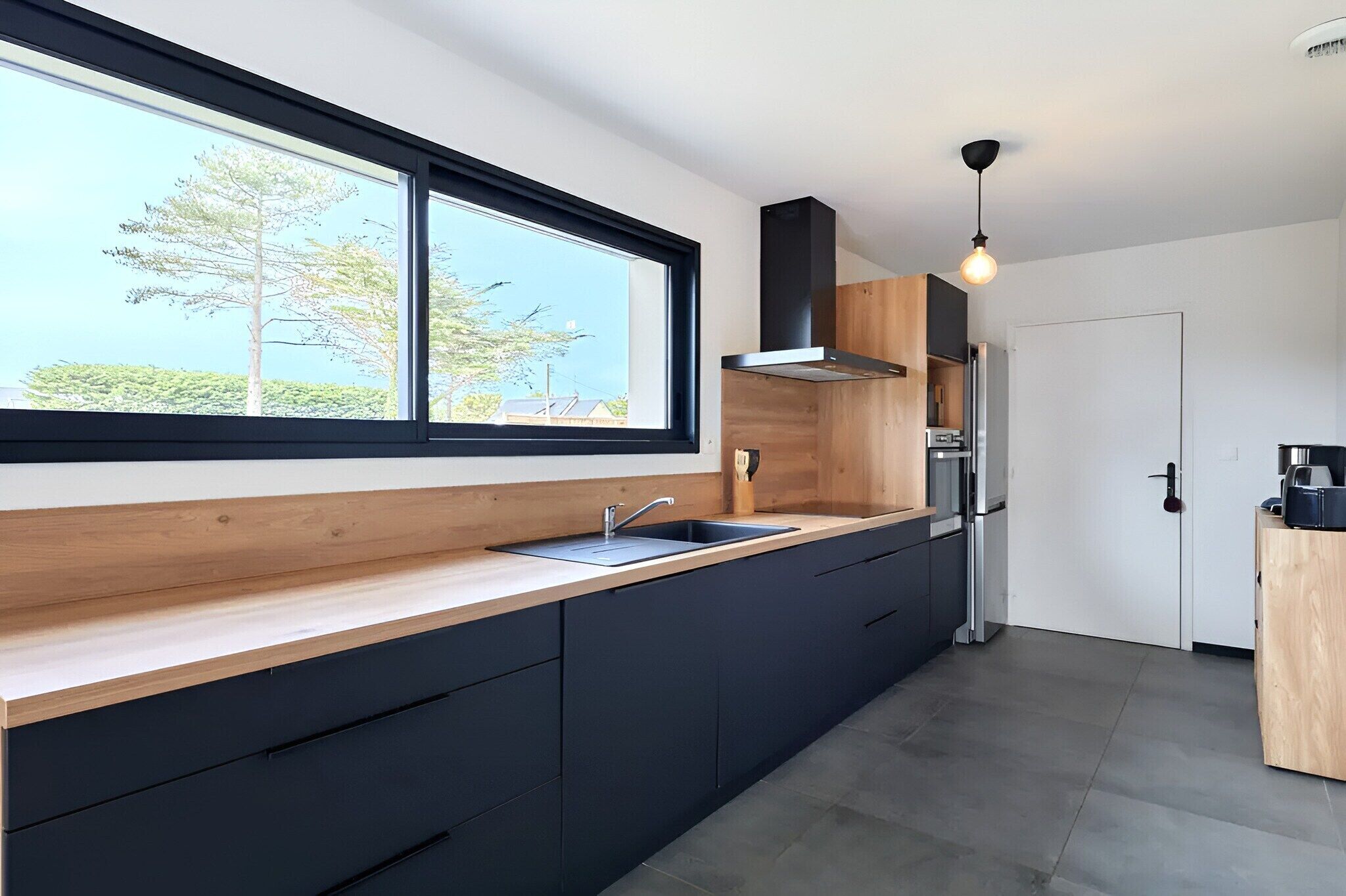 A modern kitchen with a large window, dark cabinetry, and a built-in oven.