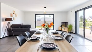 Un espace de repas moderne avec une table en bois dressée pour six personnes, un canapé, un téléviseur et une grande fenêtre.