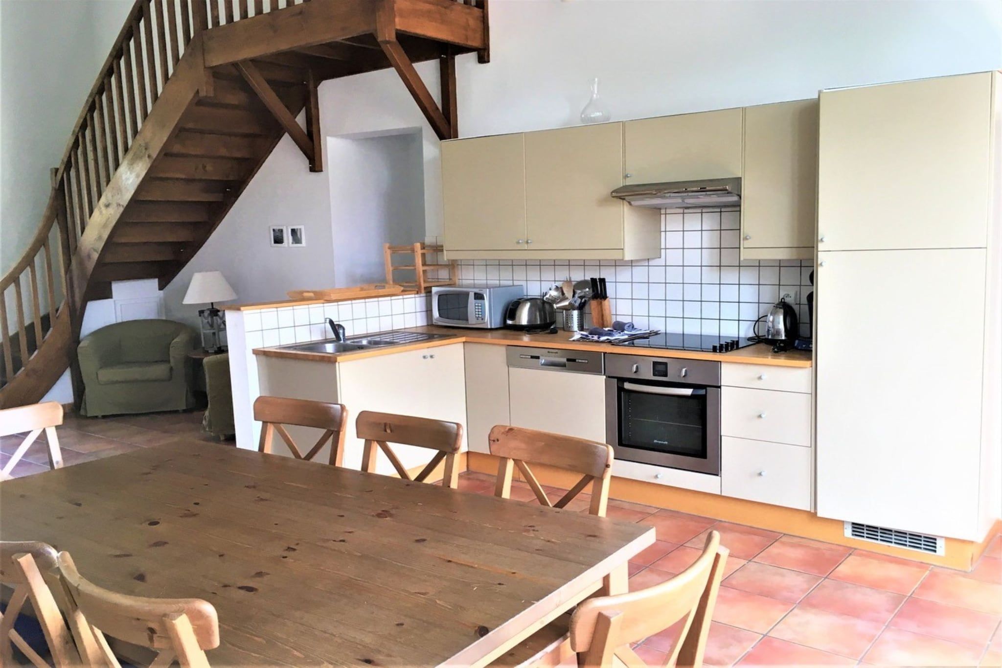 A kitchen with a wooden table and chairs, a microwave, a kettle, and a stove.