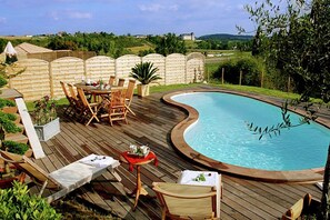 Una terraza de madera con piscina, rodeada por una valla y mobiliario exterior.