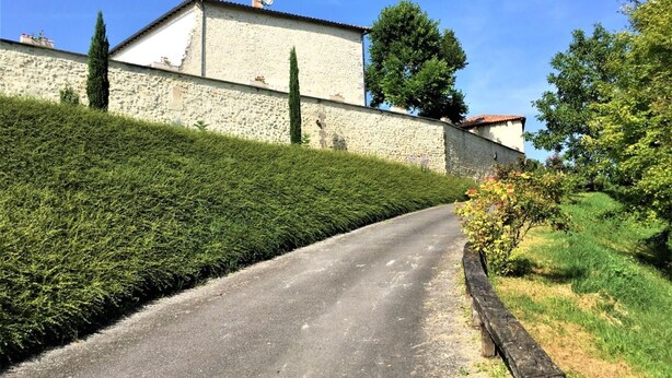 A narrow road leading to a stone building with a tiled roof, surrounded by well-maintained hedges and trees. - Villa in France with Private Pool & Garden (Chalais)