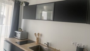 A modern kitchen with a built-in microwave, a sink, and a kettle. - Appartement T2 Avec Terrasse de 20m2 à Proximité des Plages (Étel)
