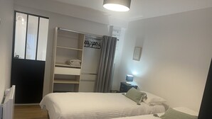 A hotel room with two beds, a wardrobe, a desk with a lamp, and a shower area. - Appartement T2 Avec Terrasse de 20m2 à Proximité des Plages (Étel)