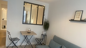 A living room with a sofa, a small table, two chairs, a mirror, and a potted plant. - Appartement T2 Avec Terrasse de 20m2 à Proximité des Plages (Étel)